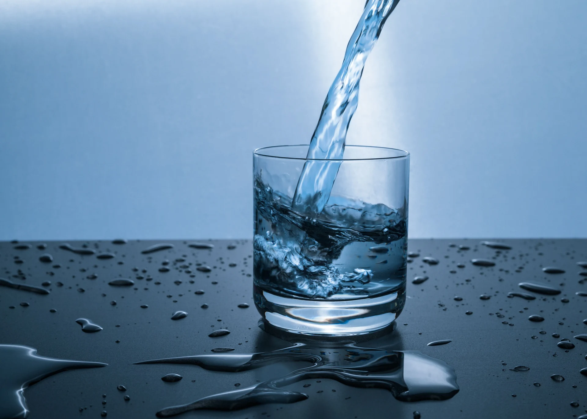 清澈的水流倒入玻璃杯,水滴落在桌面上